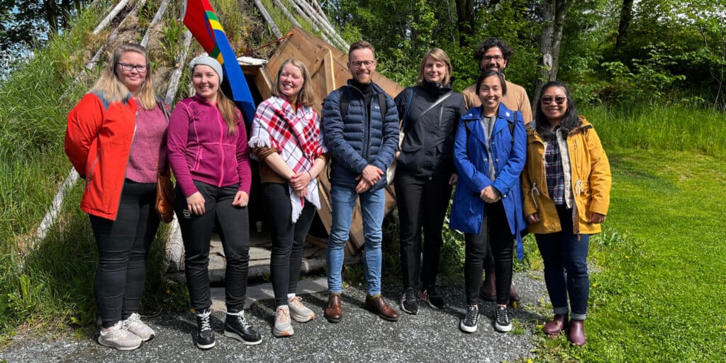 WCC Peace with Justice Pilgrimage group (Joy Eva Bohol in the yellow coat) and local hosts pose with Nord University Sami students Ramona Linnea Victoria Kappfjell Sorfijell and Maajja-Krihke Bransfjell (2nd and 3rd from L) in front of the Sami traditional hut. (Photo: Joy Eva Boho)