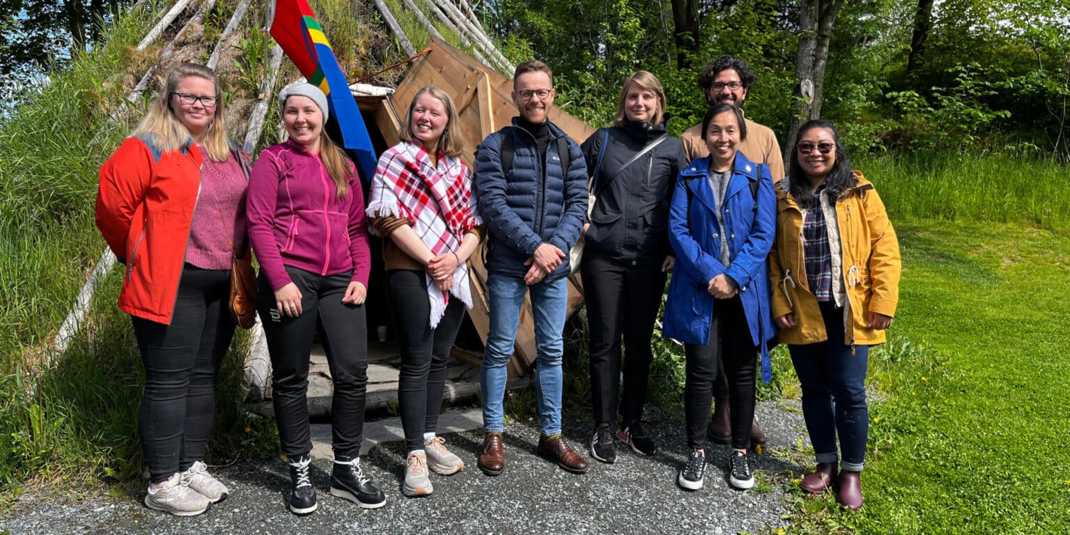WCC Peace with Justice Pilgrimage group (Joy Eva Bohol in the yellow coat) and local hosts pose with Nord University Sami students Ramona Linnea Victoria Kappfjell Sorfijell and Maajja-Krihke Bransfjell (2nd and 3rd from L) in front of the Sami traditional hut. (Photo: Joy Eva Boho)