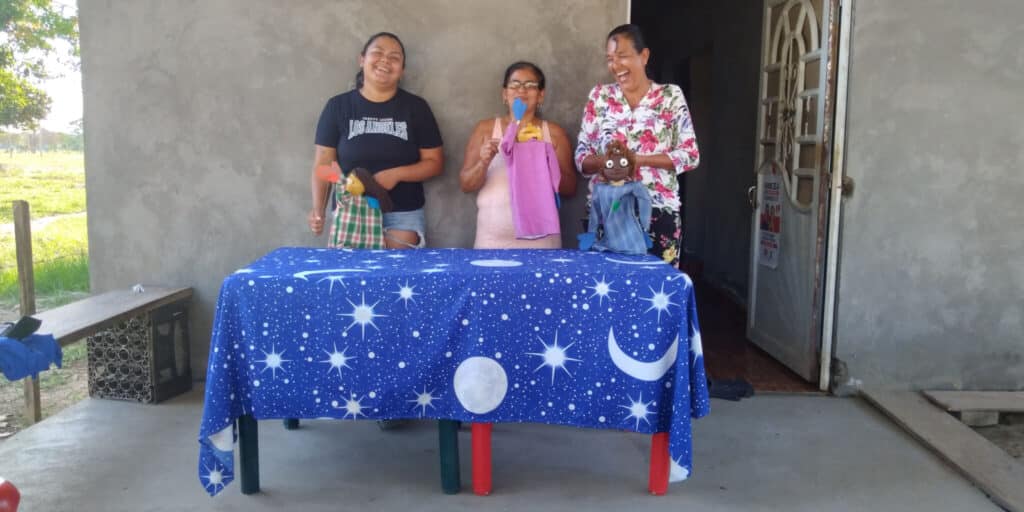 Women of the NAR La Pista community, a former FARC guerilla group in Colombia, laugh as they use CEPALC puppets to narrate a story. (Photo courtesy of CEPALC).
