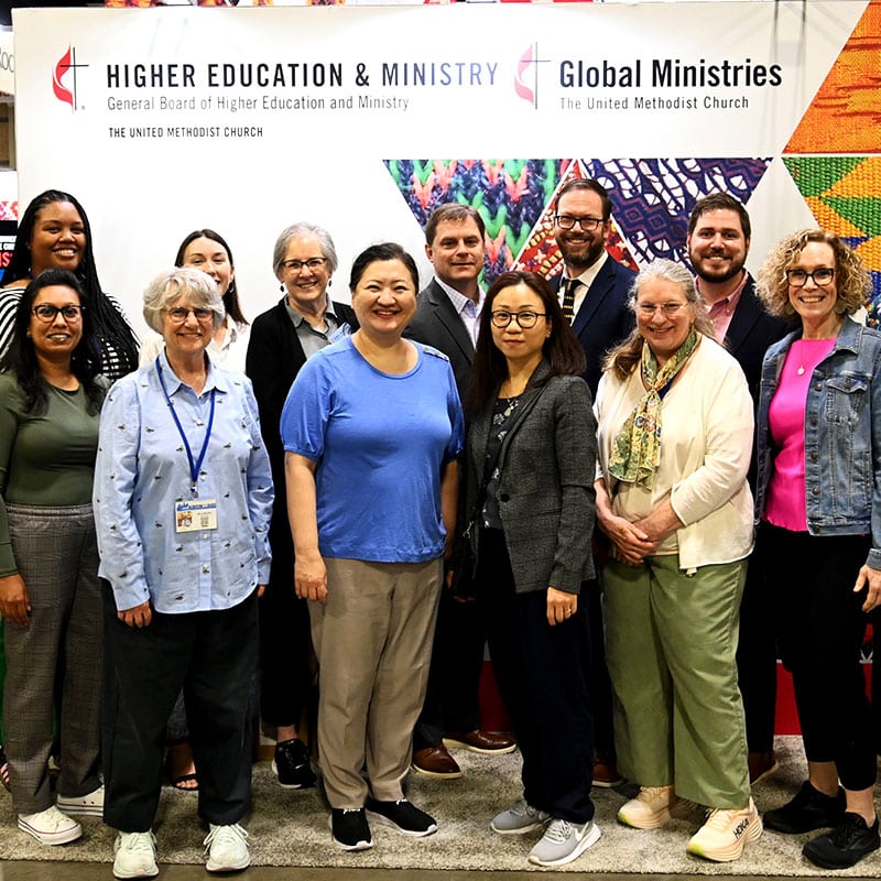 A group of Global Ministries and Higher Education and Ministry staff posing in front of the booth at General Conference in Charlotte, 2024.